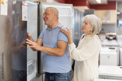 Fotografia Elderly couple stands in a hardware store and chooses a roomy refrigerator to st