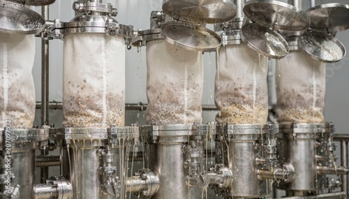 Medium shot of bag filter systems removing impurities from gum liquids focusing on filter bags within stainless steel housings amidst dynamic filtration process.