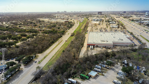 Industrial retail zones sit adjacent to dense cluster of long term trailer dwellings. Bare trees frame clear boundary between warehouse complex residential RV park sector, Plano, TX