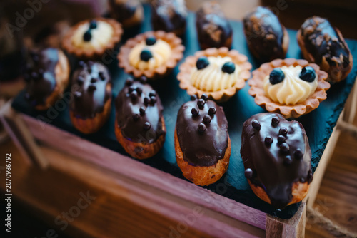 Assorted chocolate eclairs and miniature fruit tartlets set on a serving tray, featuring rich dark chocolate glaze, creamy fillings and fresh blueberries, sweet treats display for a special occasion
