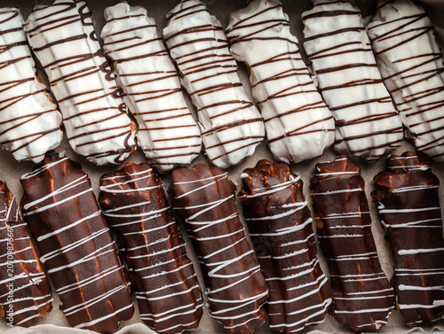 Eclairs or profiteroles with white and chocolate glaze on paper, eclair background. Sweets, dessert and pastry, close up, top view