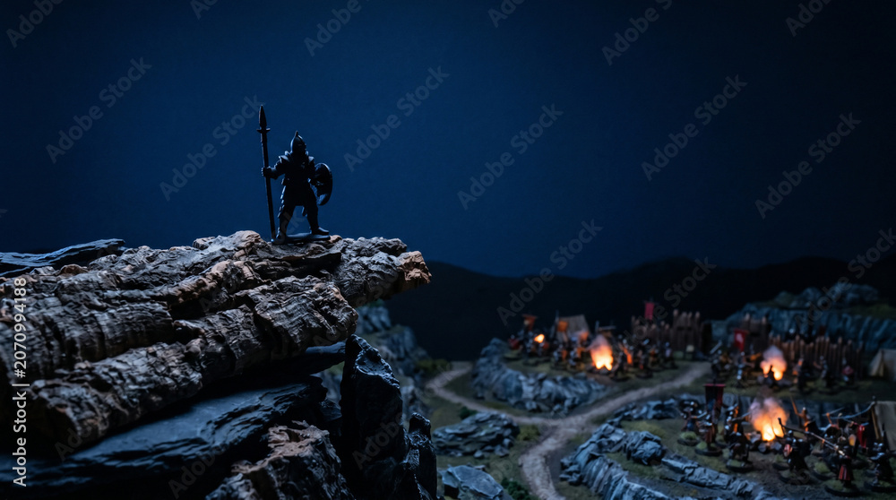 Fototapeta premium Warrior on the Cliff: A lone warrior stands atop a rocky precipice, spear in hand, surveying a village below illuminated by the eerie glow of fire and twilight.