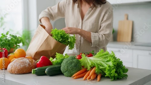 Woman unpacking healthy food and fresh organic vegetables from a paper grocery bag in the kitchen for a healthy meal