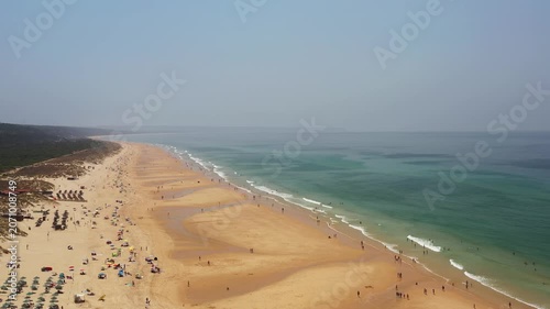 Caparica beach in Portugal where many people walk, swim, and relax on a sunny day. The sand and water are busy with different activities and sunbathers.