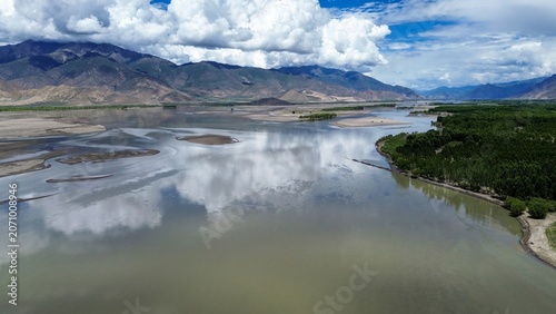 Panoramic drone view of the Yarlung Tsangpo River winding through the Lhasa valley in Tibet, flanked by mountains, sandbars, and lush green banks