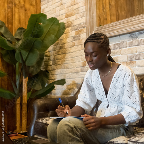 beautiful young woman woman with an african braids hairstyle studying or working with notebook and laptop