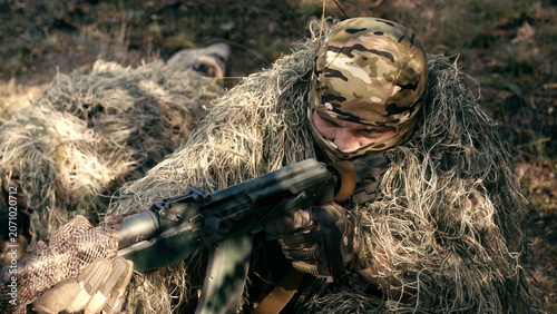 Valokuva Sniper team member in camouflage gear aiming a rifle while lying on the ground i