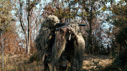 Foto Sniper team in camouflage gear carrying tactical equipment through a wooded area