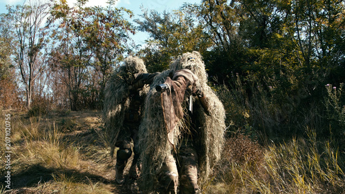 Foto Sniper team in camouflage gear carrying tactical equipment through dense foliage