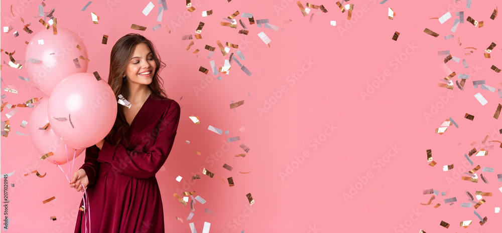 Fototapeta premium Smiling Young Woman Holding Three Pink Balloons, Enjoying Celebration At Fun Party Setting With Colorful Confetti Falling Around, Conveying Joyful And Happy Emotion, Celebration Theme.