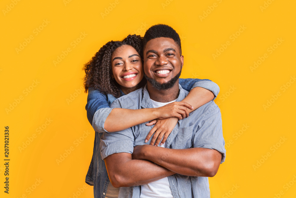 Obraz premium Smiling African American Couple In Their 20s Joyfully Embracing Each Other Against A Bright Yellow Background, Radiating Happiness And Togetherness. Perfect For Relationship And Family Concept.