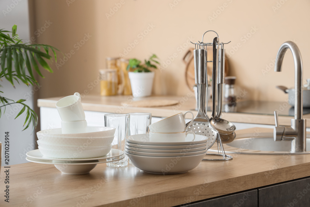 Fototapeta premium Clean white dishes and kitchen utensils on wooden countertop near sink