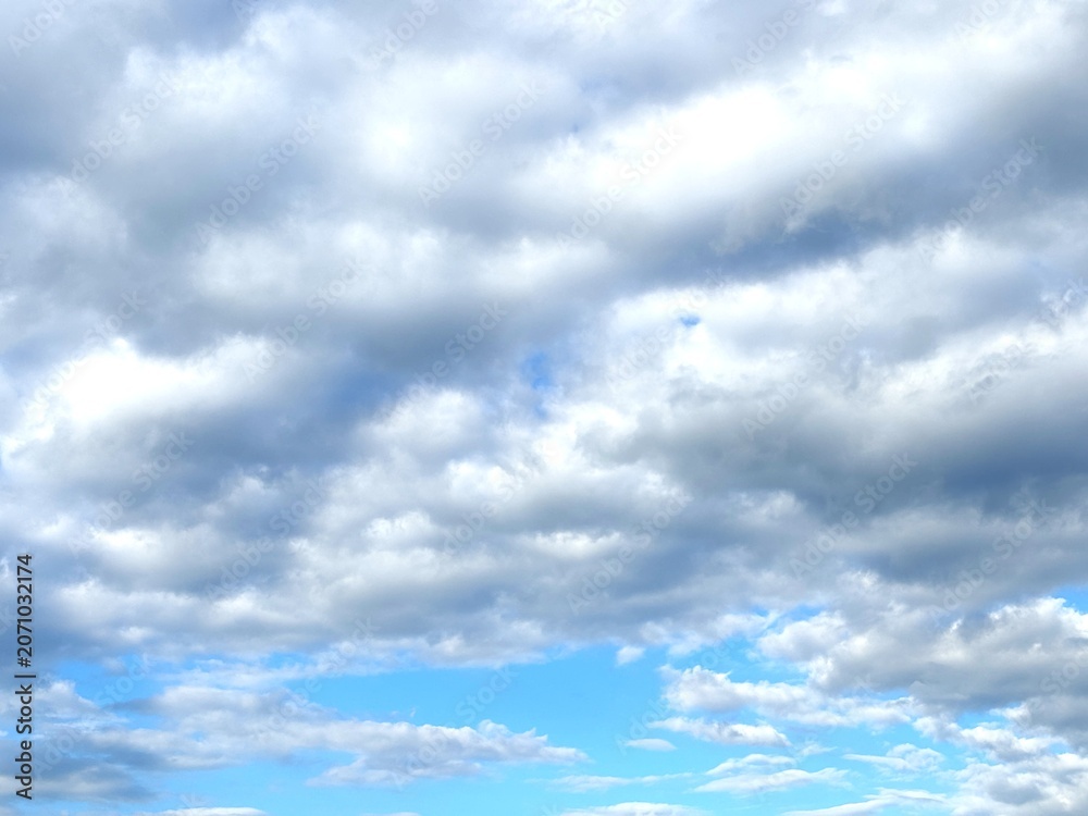Obraz premium Dramatic gray cumulus clouds cover the blue sky, creating a textured cloudscape with natural light and changing weather conditions.