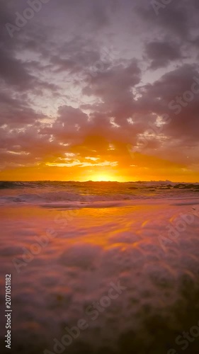 Slow motion video of gentle waves washing across the sand at sunrise as the rising sun reflects on the water at Bronte Beach, Sydney, Australia.