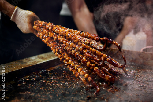 Foto Street food vendor grilling glossy ikayaki squid tentacles over a hot iron gridd