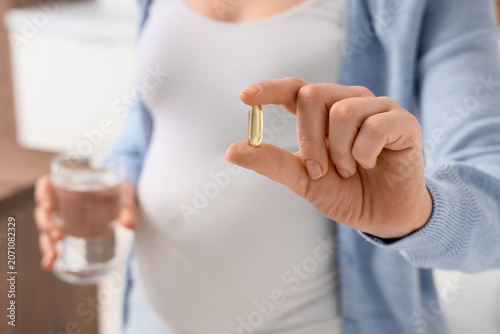 Obraz na płótnie Pregnant woman with Folic acid pill and glass of water in kitchen, closeup