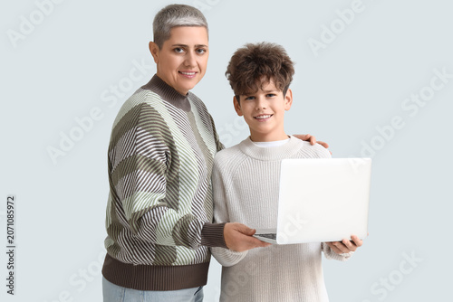 Mother and her teenage son in warm sweaters with laptop on white background