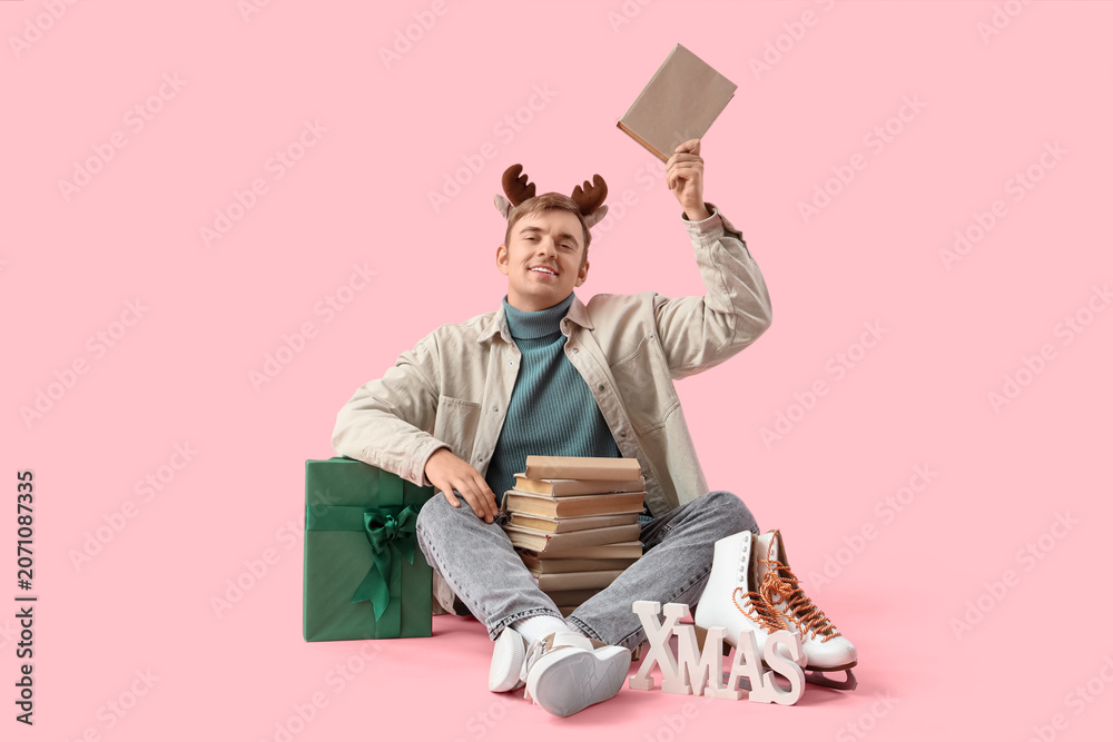 Naklejka premium Young man with many books on pink background. Christmas celebration