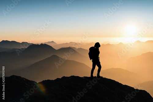 Hiker silhouette standing on a mountain peak during a vibrant sunrise adventure