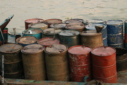 Tableau sur toile Group of rusty metal barrels stacked on dockside by river with industrial contai