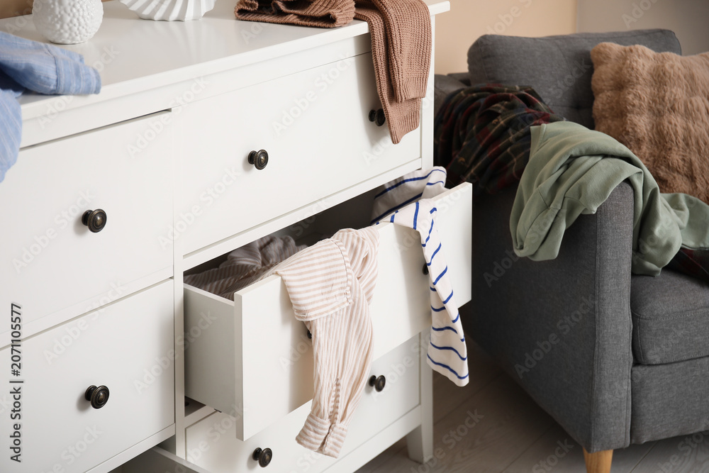 Fototapeta premium Stylish commode with different scattered clothes near beige wall in room, closeup