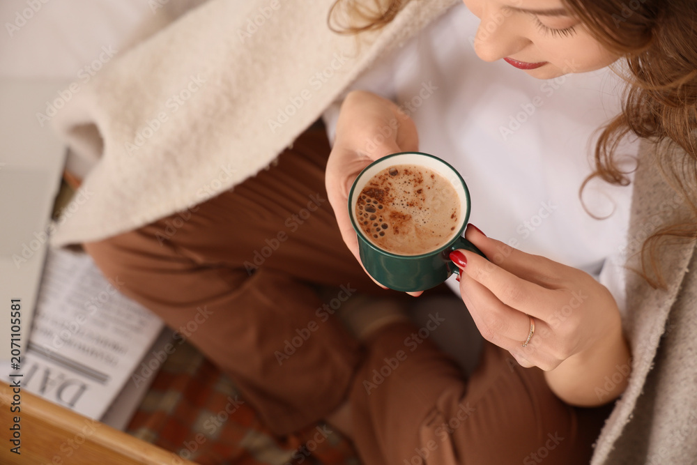 Fototapeta premium Beautiful young woman with cup of tasty coffee and plaid sitting at home, closeup