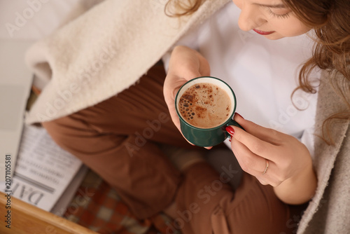 Beautiful young woman with cup of tasty coffee and plaid sitting at home, closeup