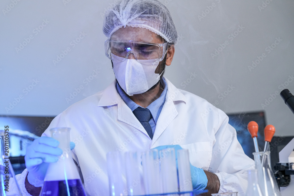 Fototapeta premium Scientists in lab coats and masks examine samples with a microscope and test tubes in a modern research laboratory.