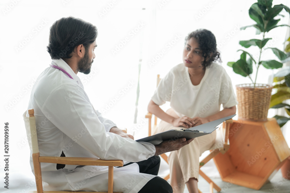 Fototapeta premium Doctor wearing a face mask examines and consults a patient during a medical checkup in a bright modern clinic.
