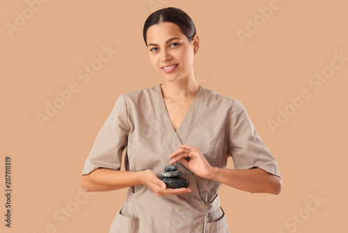 Female massage therapist with spa stones on beige background