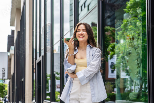 Bild auf Leinwand Happy young Asian woman walking on city street talking on smartphone using voice message