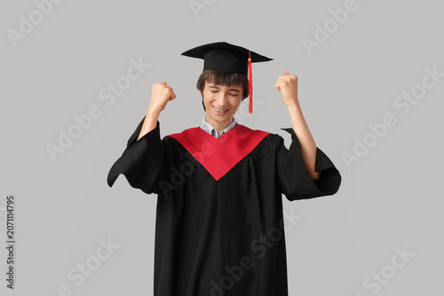 Happy male graduating student on grey background