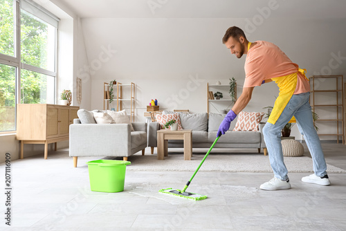 Male janitor cleaning floor with mop in light room