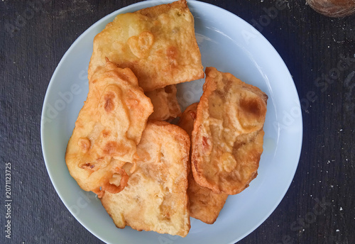 battered and fried tempe gembus served on a blue plastic plate on a dark wooden table.