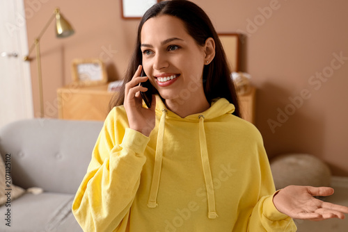Young woman in hoodie talking by mobile phone at home, closeup
