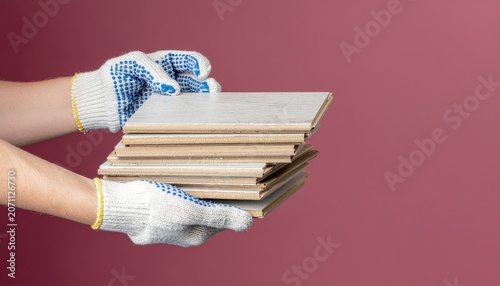 Hands in protective gloves carry stack of laminated flooring planks for installation