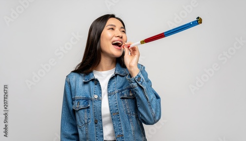 Cheerful asian woman celebrating with a party horn blower, exuding happiness