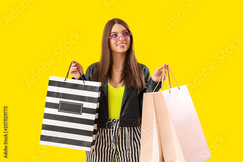 Young woman with shopping bags on yellow background
