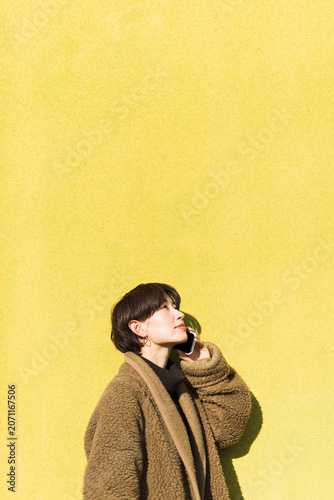 Fotografía 黄色い壁の前でスマートフォンで電話する30代女性