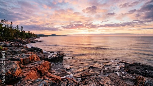 Beautiful summer sunrise painting vibrant sky above dramatic rugged rocky coastline along vast Lake Superior.