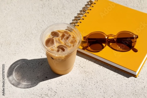 Iced Coffee, Amber Sunglasses and Yellow Notebook in Bright Summer Solstice Sunlight on Concrete