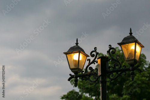 Obraz na plátně Vintage street lamps glow warmly against a cloudy evening sky