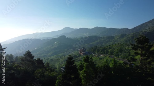 Aerial push in shot of lush green tea plantation hills and winding road under clear blue sky in Puncak, Bogor.