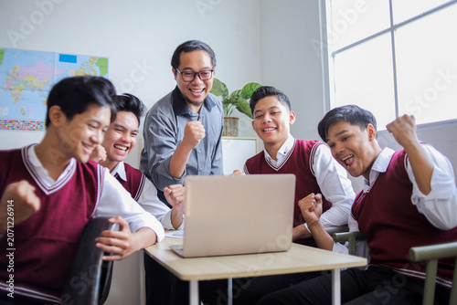 Cheerful Asian Students and Teacher Celebrating Success While Looking at laptop Screen Together