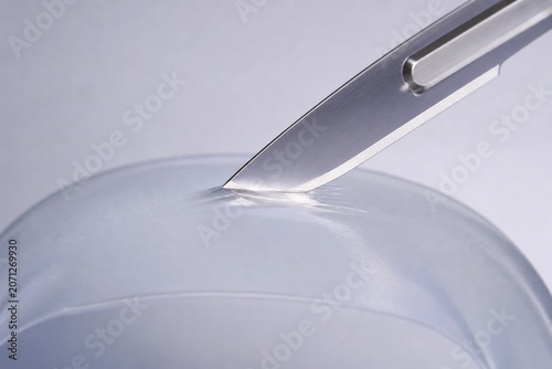 Surgical scalpel blade resting against a thin, translucent silicone membrane.