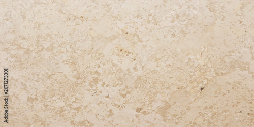 A close-up, high-angle view of a textured beige stone surface, showcasing natural variations and subtle imperfections in its granular composition, creating a warm and earthy backdrop.