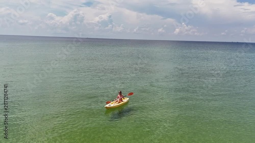 Woman kayaking alone in clear green water under a sunny sky