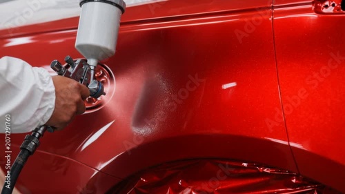 Close up of professional car spray painting shiny red automotive bodywork in workshop