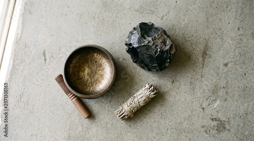 Tibetan singing bowl obsidian rock and sage smudge stick on concrete surface for meditation and cleansing rituals.