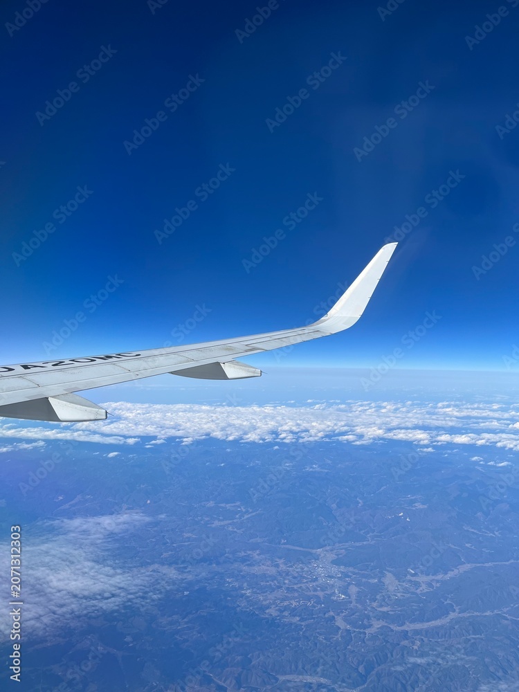 Obraz premium Airplane wing above clouds and blue sky during flight